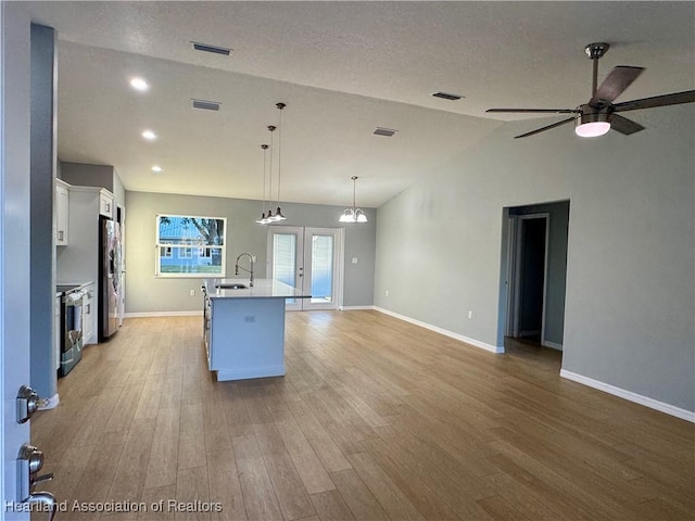 kitchen featuring lofted ceiling, pendant lighting, white cabinetry, an island with sink, and stainless steel appliances