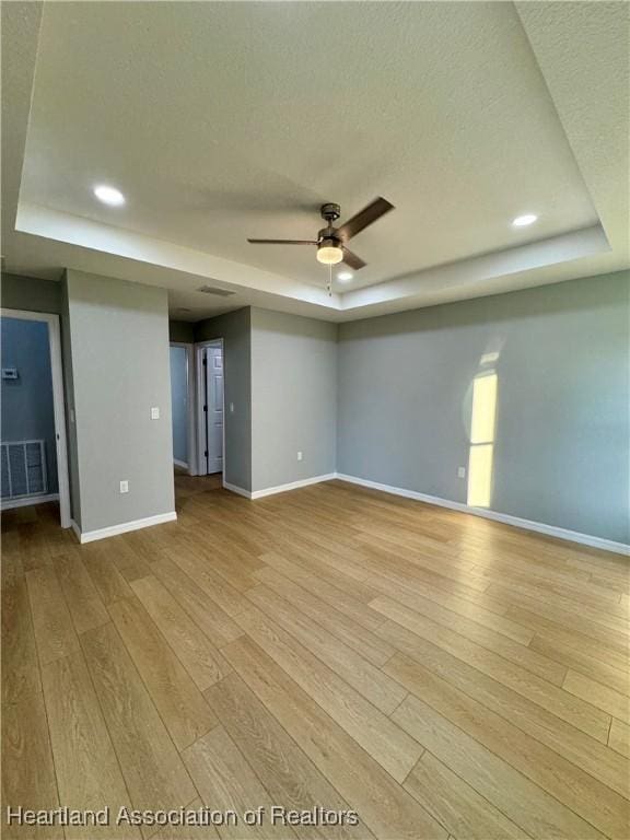 unfurnished room featuring light hardwood / wood-style floors, a raised ceiling, and ceiling fan