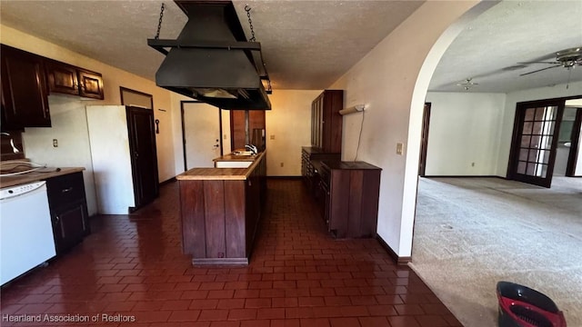 kitchen with island range hood, arched walkways, a ceiling fan, white dishwasher, and dark brown cabinets