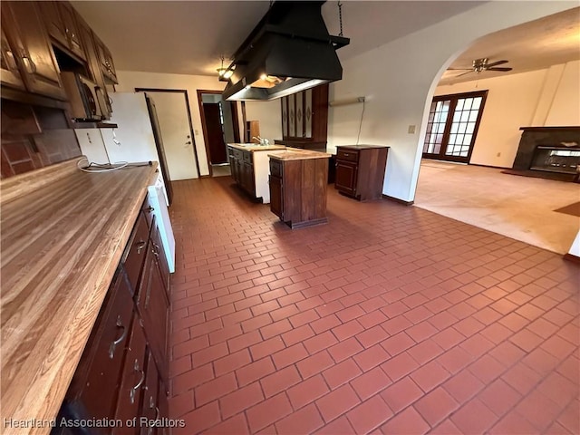 kitchen with island range hood, arched walkways, open floor plan, brick floor, and light countertops