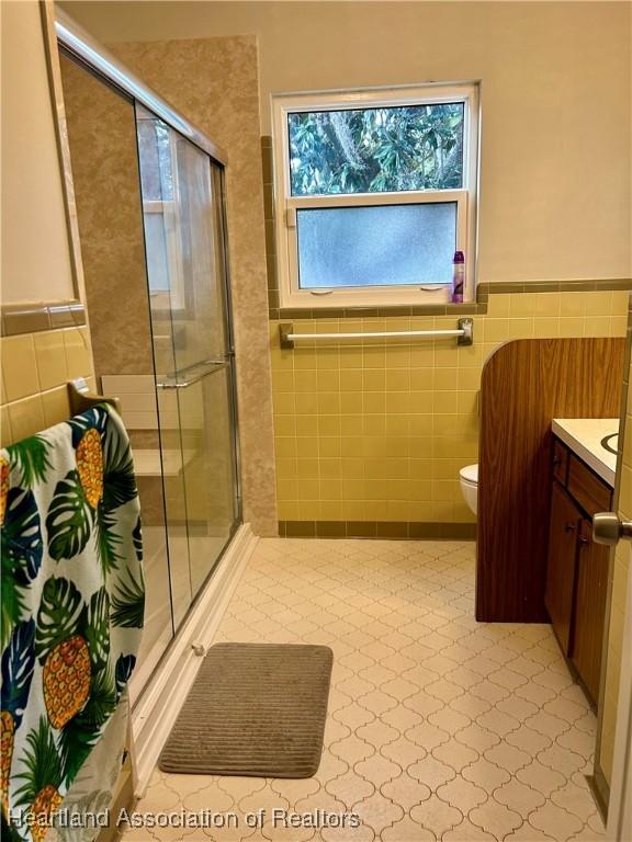 bathroom with toilet, tile walls, an enclosed shower, and vanity