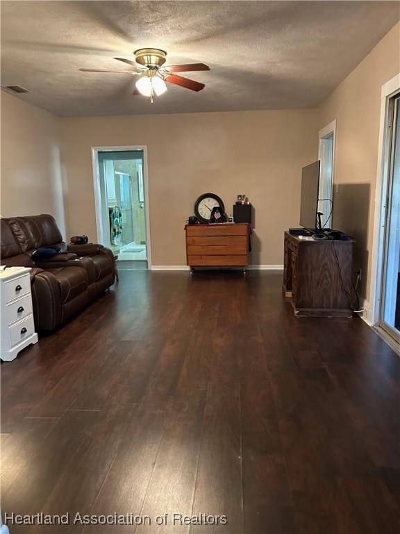 living room featuring dark hardwood / wood-style flooring, ceiling fan, and a textured ceiling