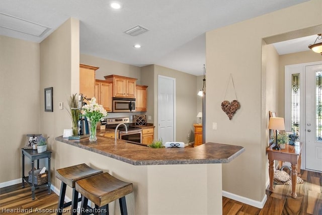 kitchen featuring a breakfast bar area, dark hardwood / wood-style floors, light brown cabinetry, kitchen peninsula, and stainless steel appliances