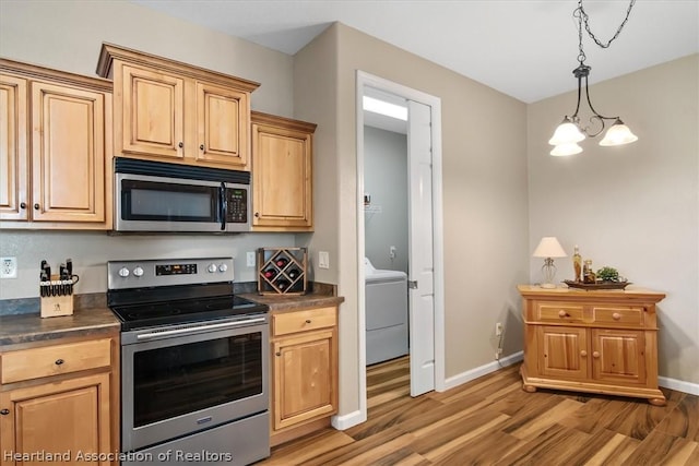 kitchen with appliances with stainless steel finishes, light hardwood / wood-style flooring, a chandelier, washer / dryer, and hanging light fixtures