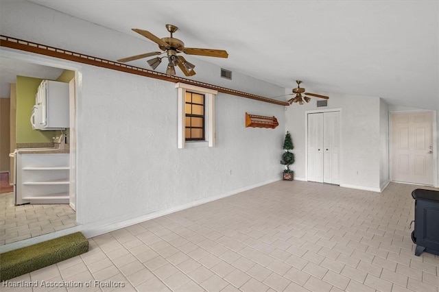 unfurnished living room featuring a wood stove, ceiling fan, and vaulted ceiling