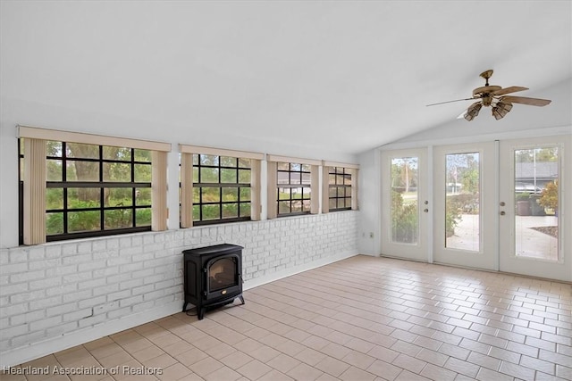 unfurnished living room featuring french doors, brick wall, ceiling fan, a wood stove, and lofted ceiling