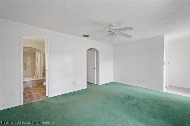 empty room with a textured ceiling, dark carpet, and ceiling fan