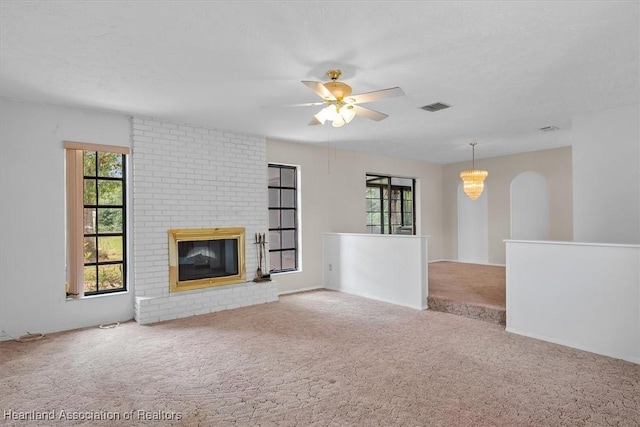 unfurnished living room featuring a fireplace, carpet, and ceiling fan with notable chandelier