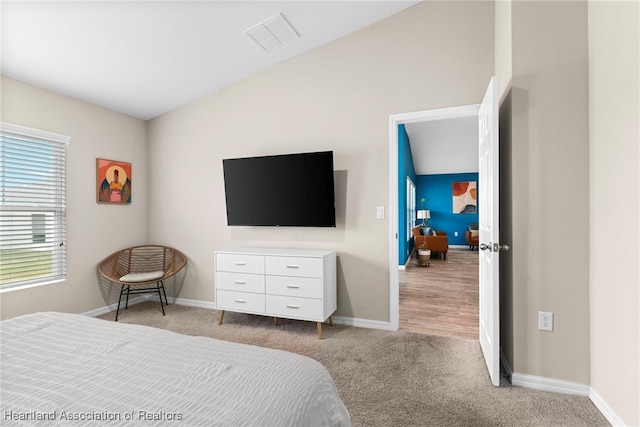 bedroom featuring light colored carpet, visible vents, lofted ceiling, and baseboards