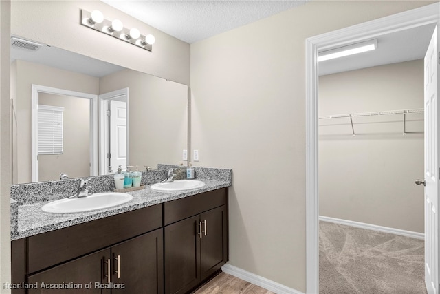 full bath with double vanity, visible vents, a walk in closet, and a sink