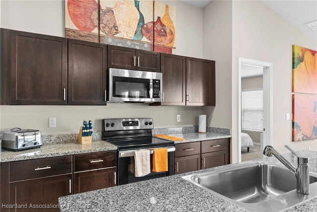 kitchen with light stone counters, appliances with stainless steel finishes, a sink, and dark brown cabinetry