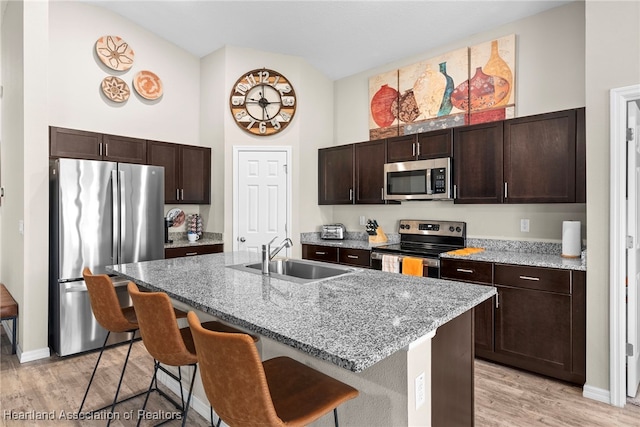 kitchen featuring a kitchen breakfast bar, stainless steel appliances, dark brown cabinets, light wood-type flooring, and a sink