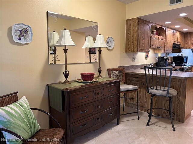6000 Matanzas Dr, Sebring, FL 33872 - kitchen with black microwave, under cabinet range hood, light tile patterned floors, dark countertops, and a breakfast bar