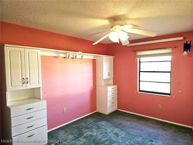 unfurnished bedroom featuring ceiling fan, dark carpet, and a textured ceiling