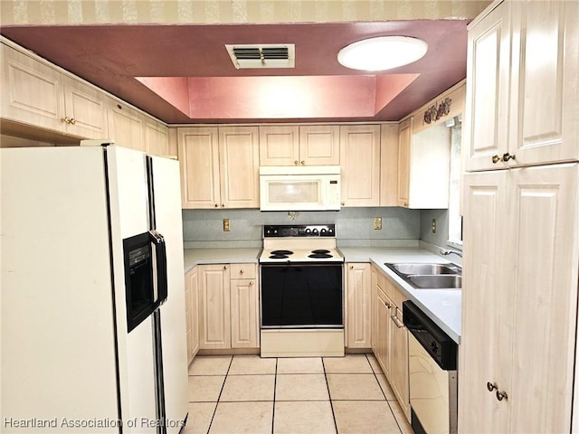 kitchen with white appliances, sink, light tile patterned floors, and a tray ceiling