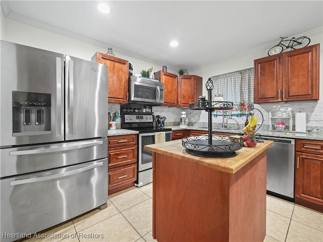 kitchen with a kitchen island, light tile patterned floors, ornamental molding, and appliances with stainless steel finishes