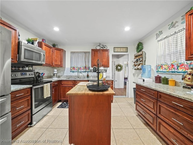 kitchen featuring light stone countertops, a center island, crown molding, light tile patterned floors, and appliances with stainless steel finishes