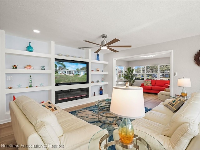 living room with built in shelves, ceiling fan, hardwood / wood-style floors, and a textured ceiling