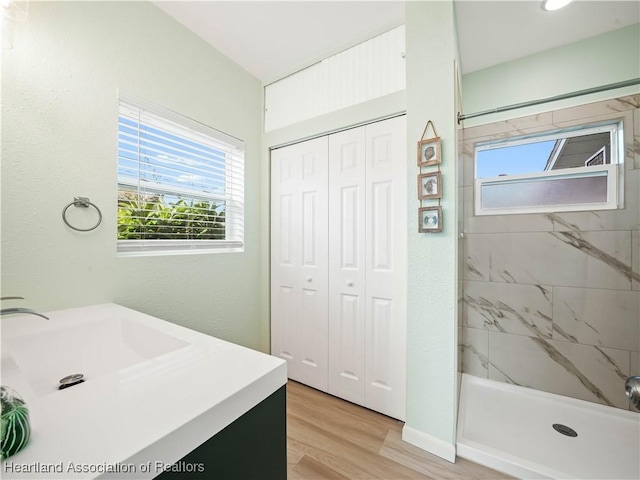 bathroom with hardwood / wood-style flooring, vanity, and a tile shower