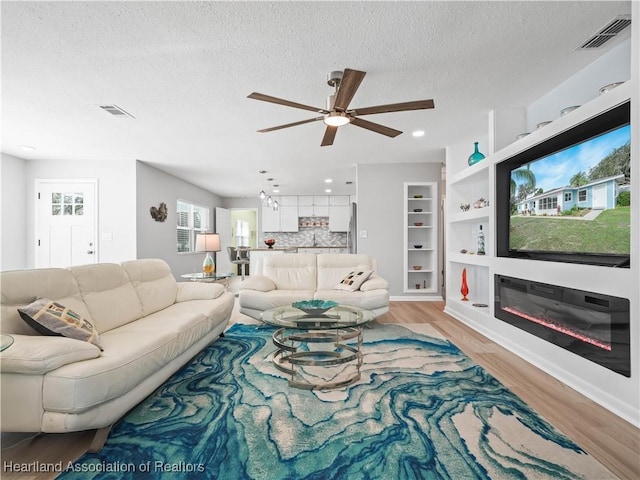 living room with ceiling fan, light hardwood / wood-style flooring, and a textured ceiling