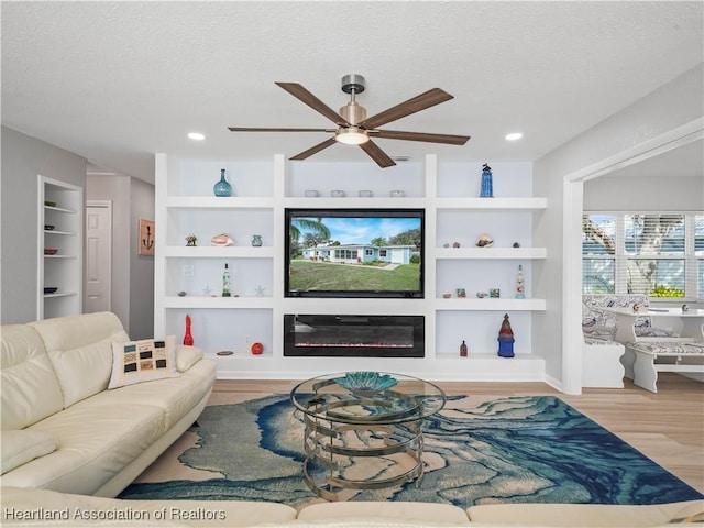 living room featuring wood-type flooring, ceiling fan, built in features, and a textured ceiling