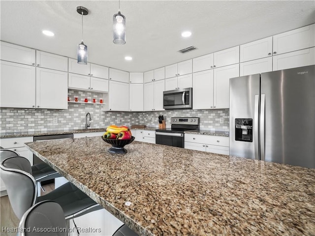 kitchen featuring a breakfast bar, sink, dark stone counters, stainless steel appliances, and white cabinets