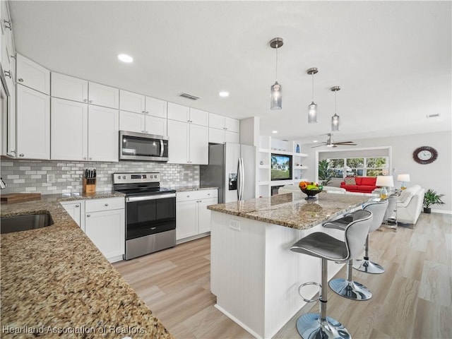 kitchen with sink, stainless steel appliances, a center island, white cabinets, and decorative light fixtures