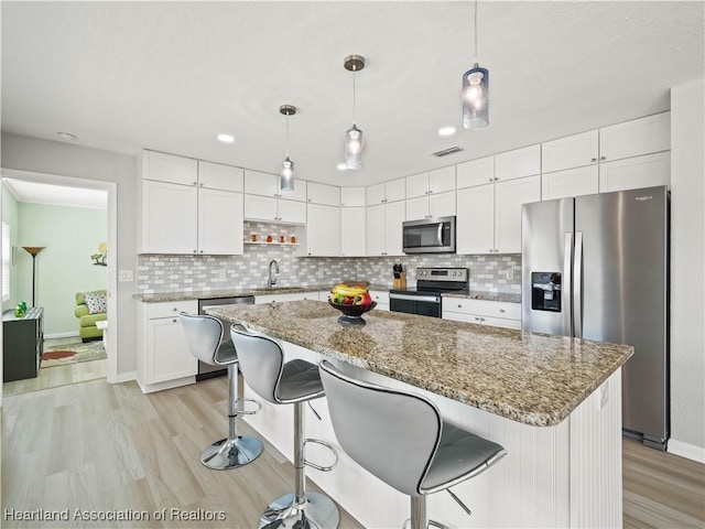 kitchen with white cabinetry, decorative light fixtures, a kitchen island, and appliances with stainless steel finishes