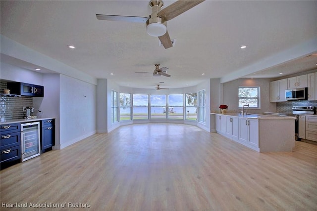 kitchen with appliances with stainless steel finishes, light wood-type flooring, beverage cooler, sink, and white cabinetry