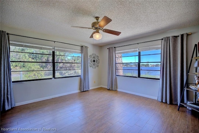 empty room with ceiling fan, hardwood / wood-style floors, a water view, and a textured ceiling