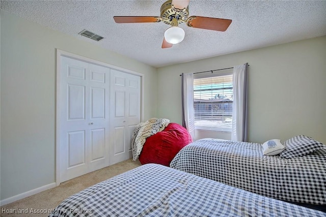 bedroom with ceiling fan, light colored carpet, a textured ceiling, and a closet