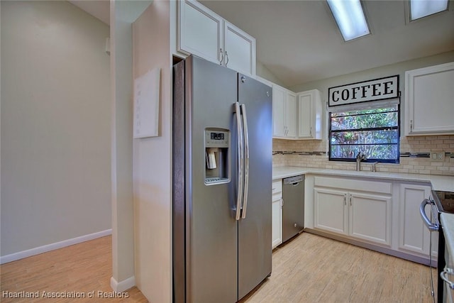 kitchen with decorative backsplash, appliances with stainless steel finishes, white cabinets, light hardwood / wood-style floors, and lofted ceiling