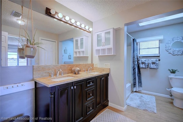 full bathroom featuring wood-type flooring, a textured ceiling, toilet, vanity, and shower / tub combo