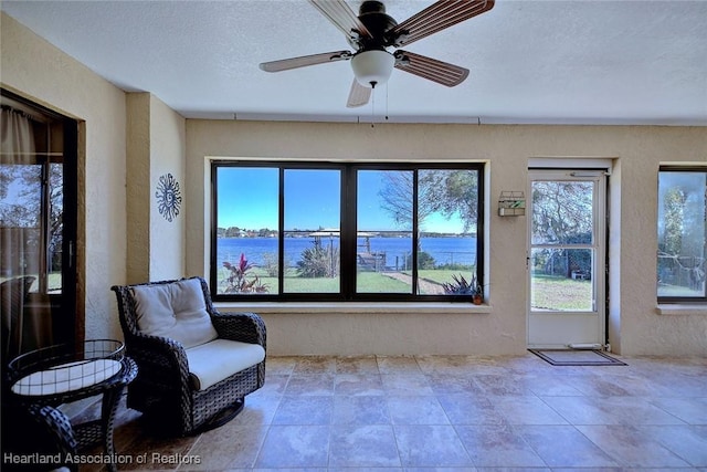 sitting room with ceiling fan, a water view, and a textured ceiling