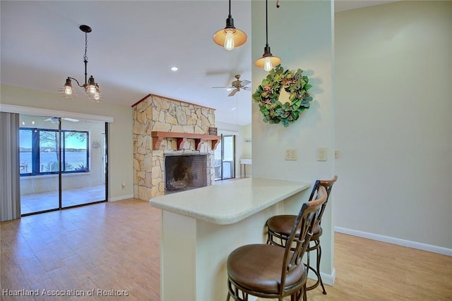 kitchen with a kitchen breakfast bar, a stone fireplace, kitchen peninsula, decorative light fixtures, and ceiling fan with notable chandelier