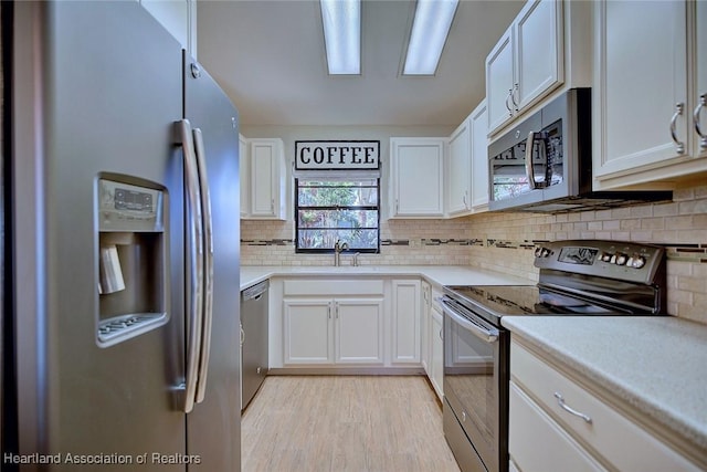 kitchen with backsplash, sink, light wood-type flooring, white cabinetry, and stainless steel appliances