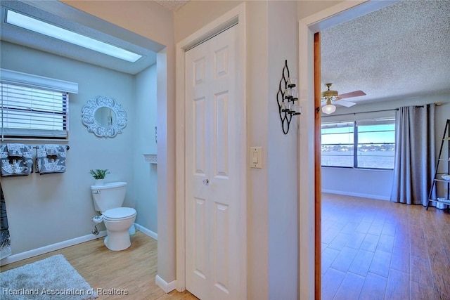 bathroom with wood-type flooring, a textured ceiling, toilet, and ceiling fan