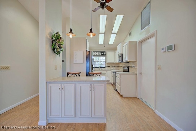 kitchen featuring white cabinets, hanging light fixtures, vaulted ceiling with skylight, decorative backsplash, and appliances with stainless steel finishes