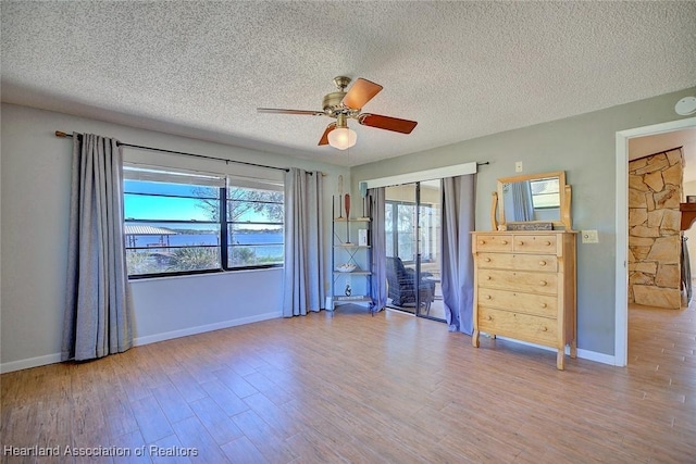 unfurnished room with ceiling fan, a textured ceiling, and light wood-type flooring