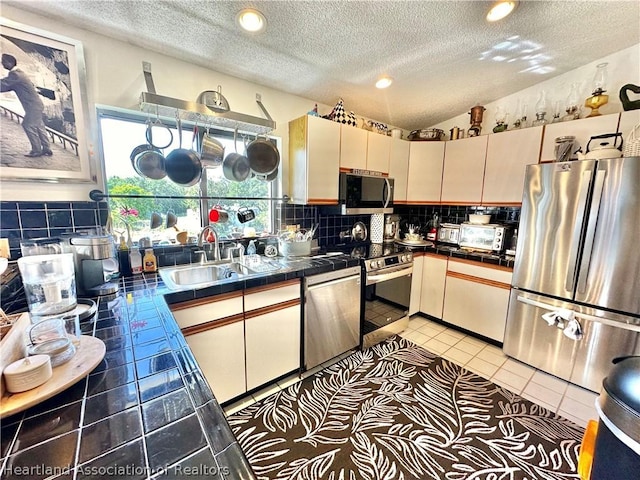 kitchen with decorative backsplash, a textured ceiling, stainless steel appliances, sink, and light tile patterned floors