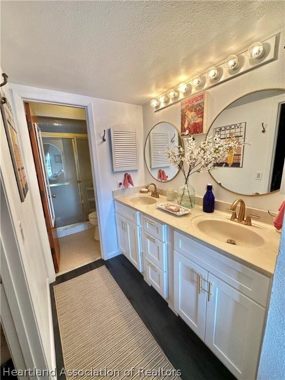 bathroom with vanity, toilet, a shower with door, and a textured ceiling