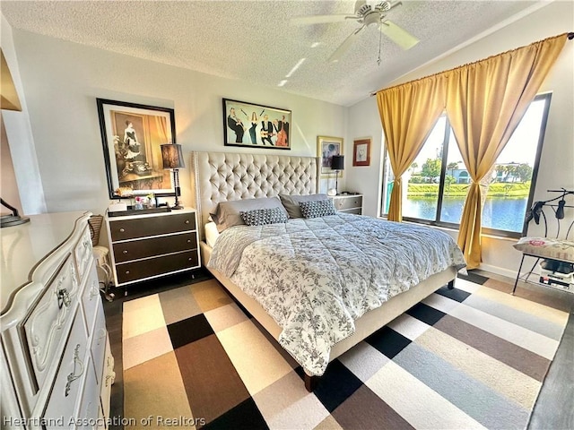 bedroom featuring a textured ceiling, a water view, ceiling fan, and lofted ceiling