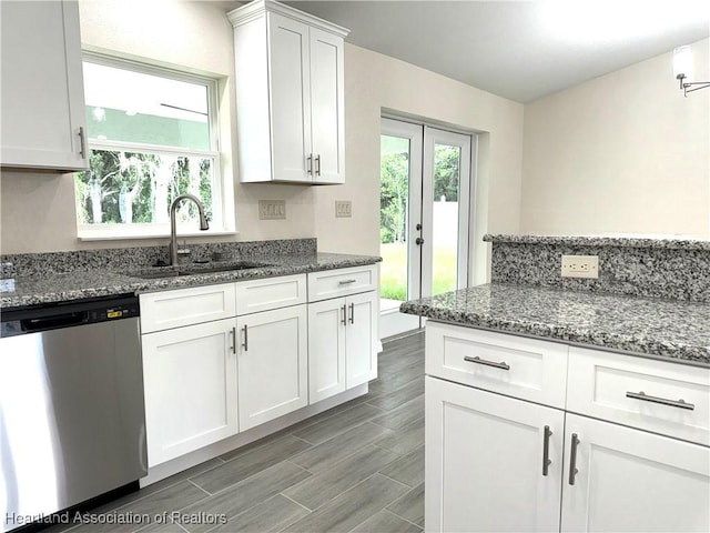 kitchen featuring stainless steel dishwasher, dark stone countertops, white cabinetry, and sink