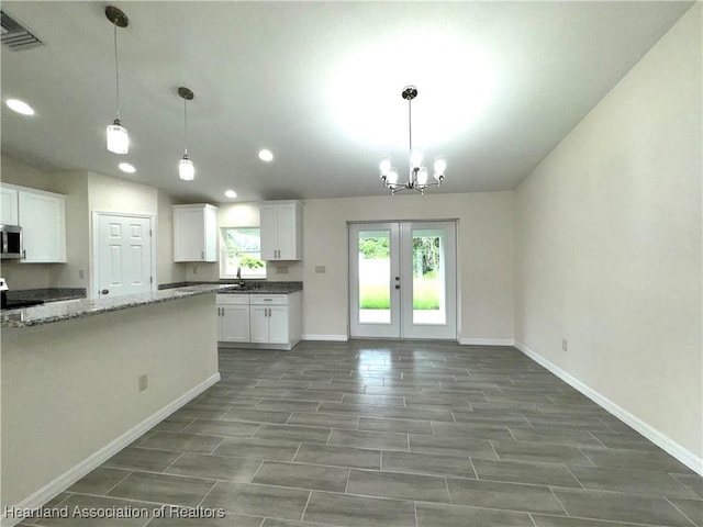 kitchen featuring light stone countertops, pendant lighting, an inviting chandelier, and white cabinetry