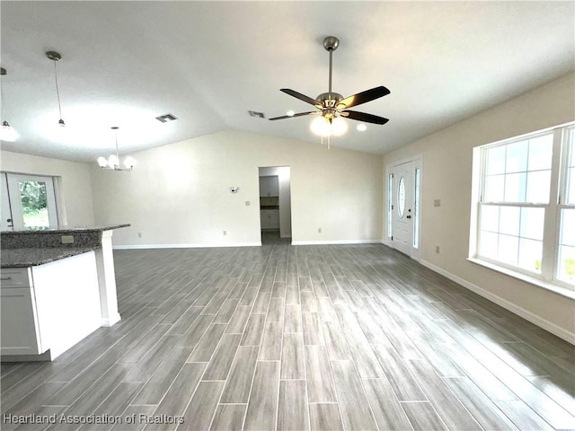 unfurnished living room with vaulted ceiling, dark wood-type flooring, and ceiling fan with notable chandelier