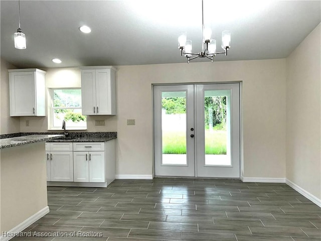 kitchen with white cabinetry, sink, a notable chandelier, dark stone countertops, and decorative light fixtures