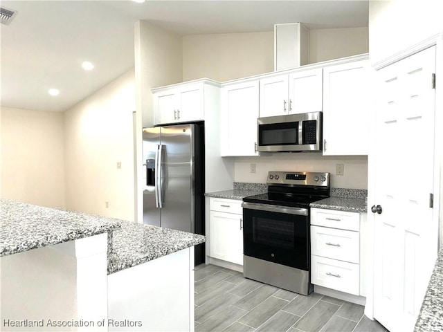 kitchen featuring light stone countertops, appliances with stainless steel finishes, vaulted ceiling, and white cabinetry