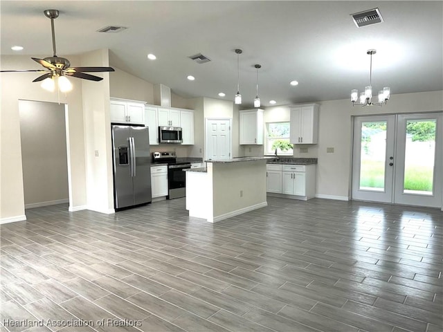 kitchen with appliances with stainless steel finishes, decorative light fixtures, a center island, white cabinetry, and lofted ceiling