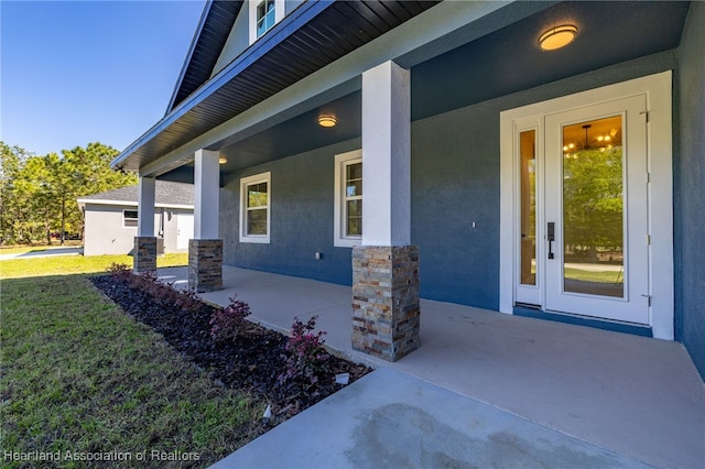 property entrance with stucco siding, stone siding, a yard, and a porch