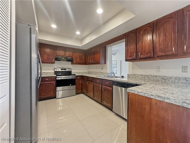 kitchen featuring light stone countertops, stainless steel appliances, a tray ceiling, sink, and light tile patterned floors